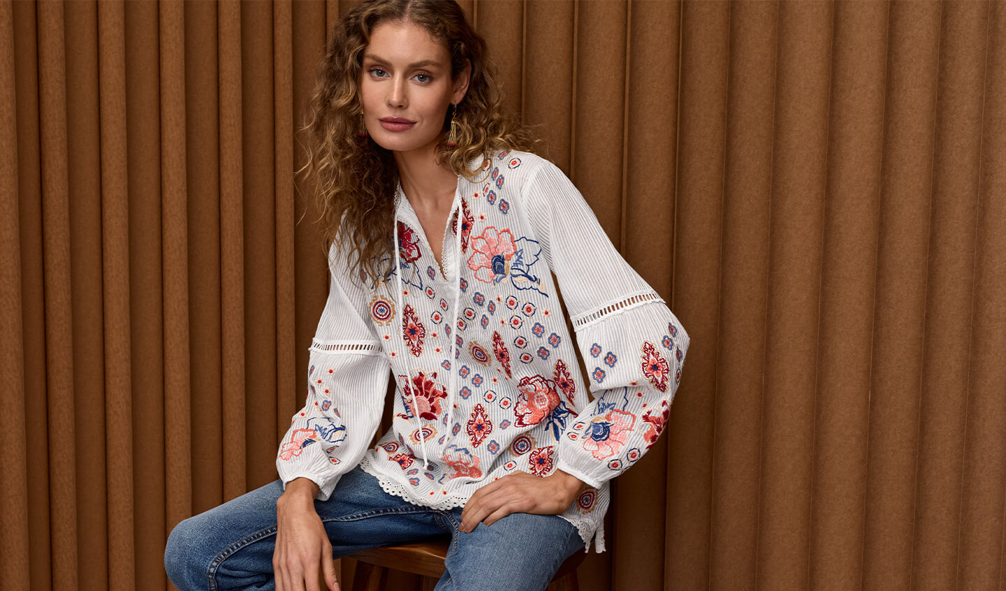 Model sitting wearing a embroidered white blouse