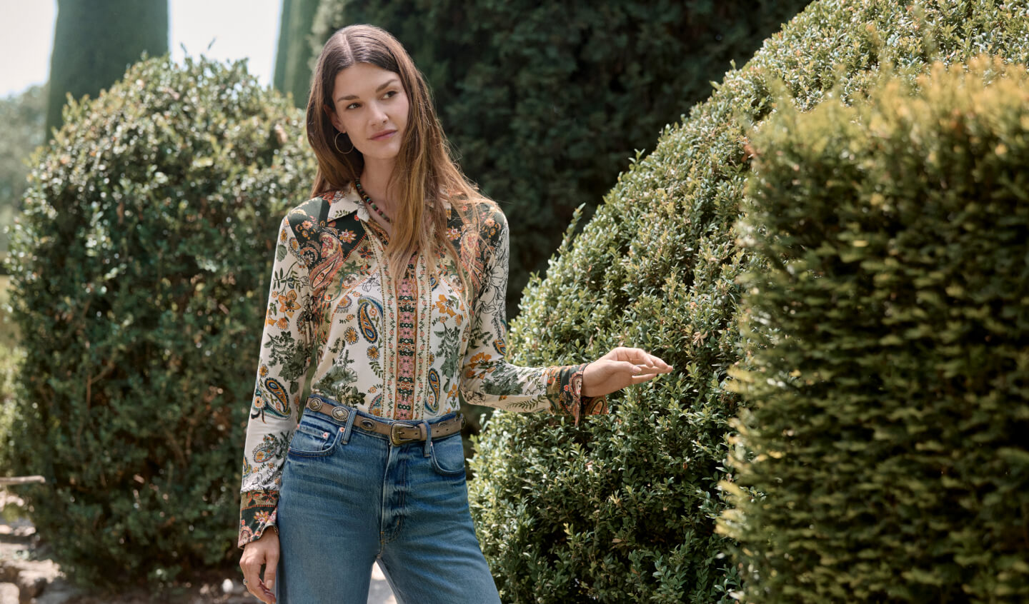 Model standing wearing prints long sleeve blouse with a leather belt and jeans
