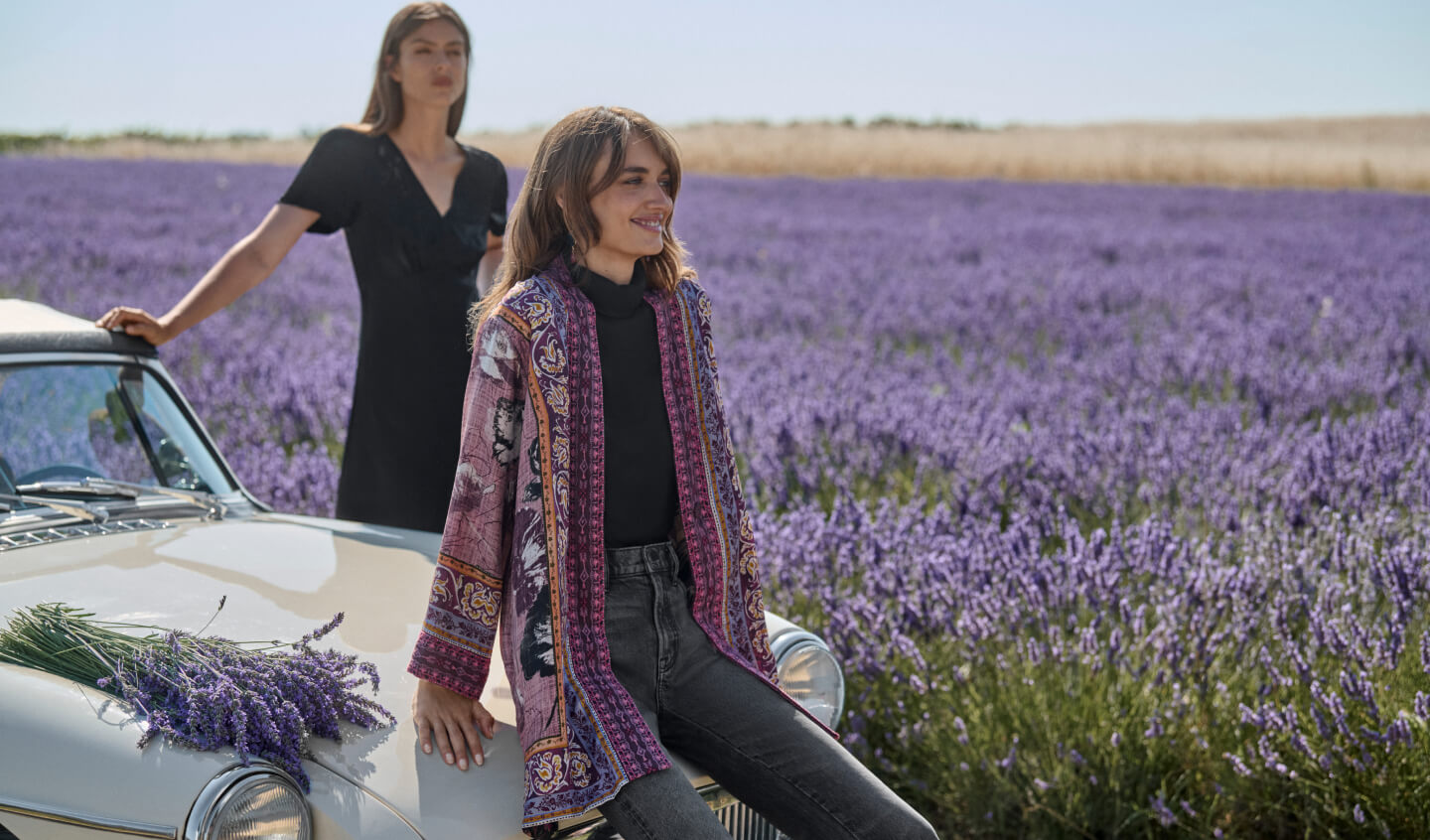 Two Models by white car, one sitting with printed kimono the other standing in a black dress