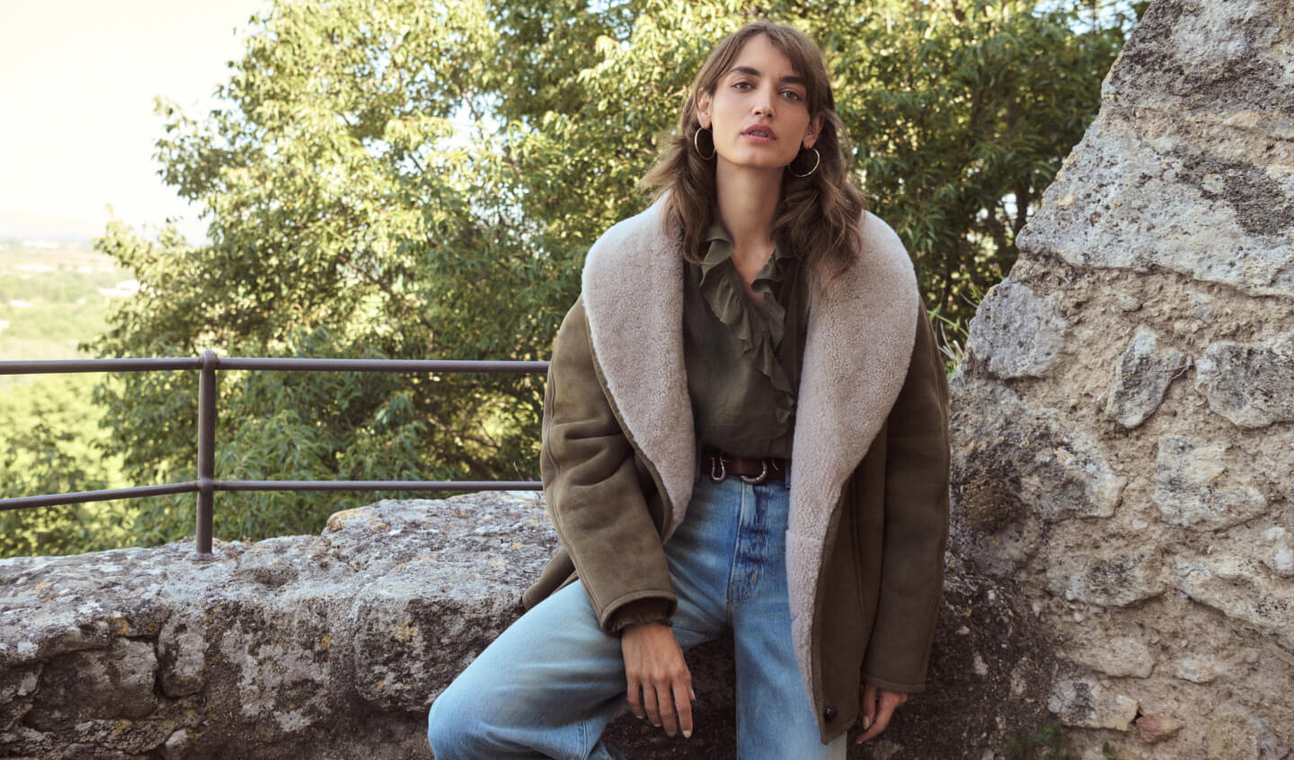 Model sitting wearing green blouse with suede jacket and jeans