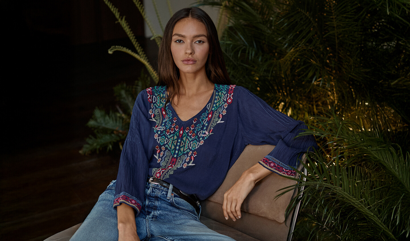 Model sitting wearing a embroidered navy blouse