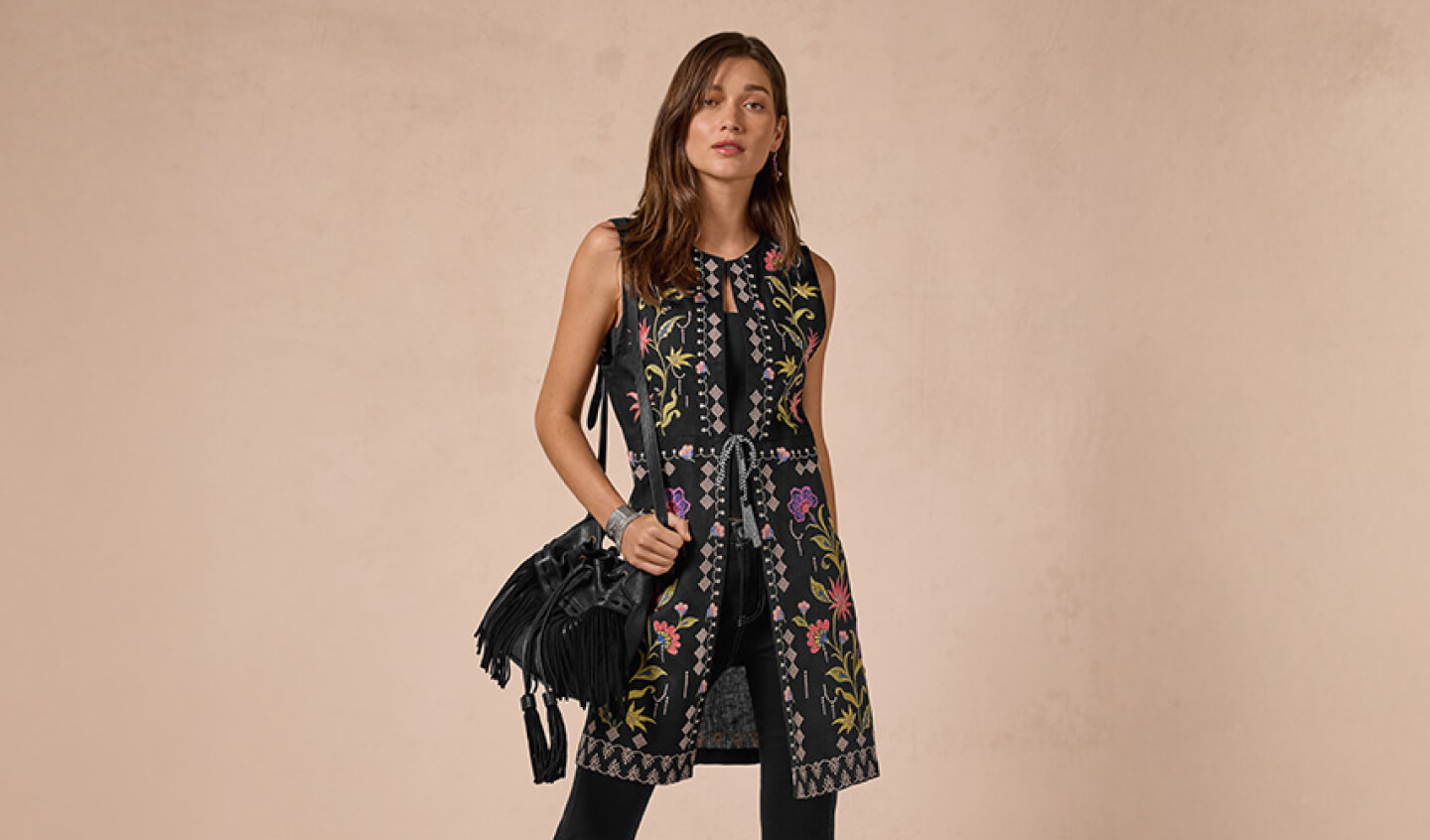 Model wearing a black embroidered best with a black leather handbag