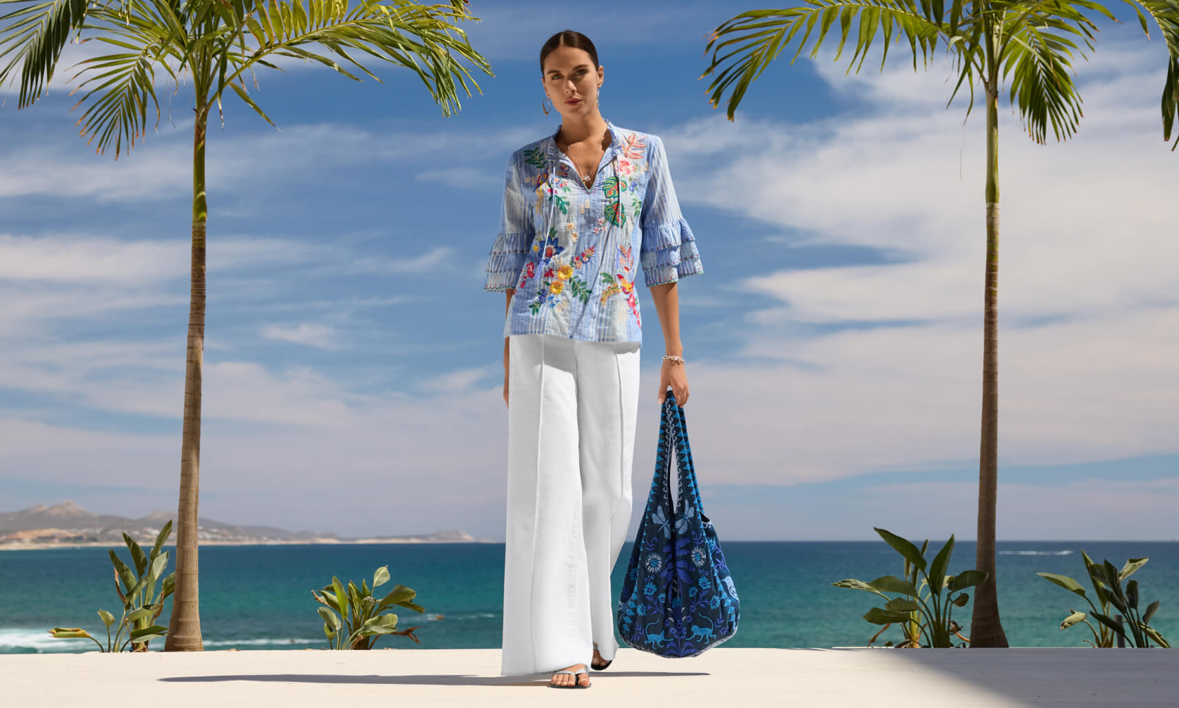 Model wearing embroidered top and white jeans with a blue embroidered bag